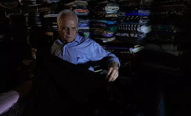 A textile seller works at his shop during power outage in Tehran, Iran, Tuesday, Aug. 5, 2025. (AP Photo/Vahid Salemi)