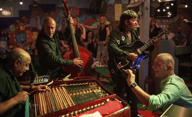 A customer records video as Tudor Lakatos, right, who goes by the stage name Elvis Rromano, performs at the Terasa Florilor restaurant, along with Nicolae Feraru, left, and Stefan Marin, center, of the Taraful Frunzelor band, in Bucharest, Romania, Friday, June 20, 2025.(AP Photo/Vadim Ghirda)