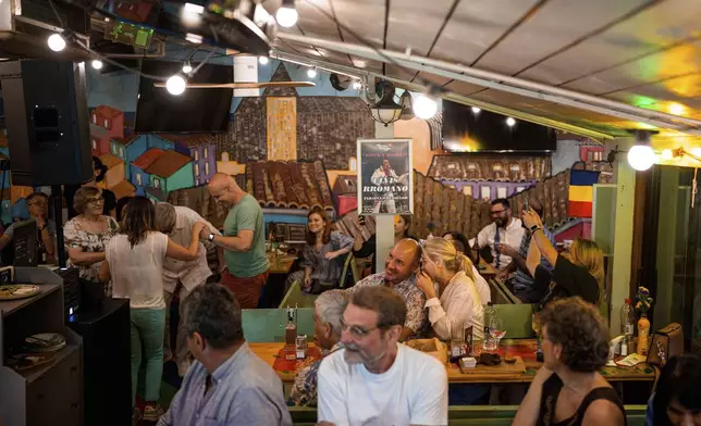 A poster advertising his concert of Tudor Lakatos, who goes by the stage name Elvis Rromano, sits on a pole as customers enjoy the show at the Terasa Florilor restaurant before a performance in Bucharest, Romania, Friday, June 20, 2025. (AP Photo/Andreea Alexandru)