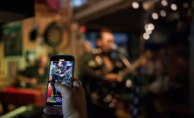 A customer records video of Tudor Lakatos, who goes by the stage name Elvis Rromano, performing at the Terasa Florilor restaurant with the Taraful Frunzelor band, in Bucharest, Romania, Friday, June 20, 2025. (AP Photo/Andreea Alexandru)