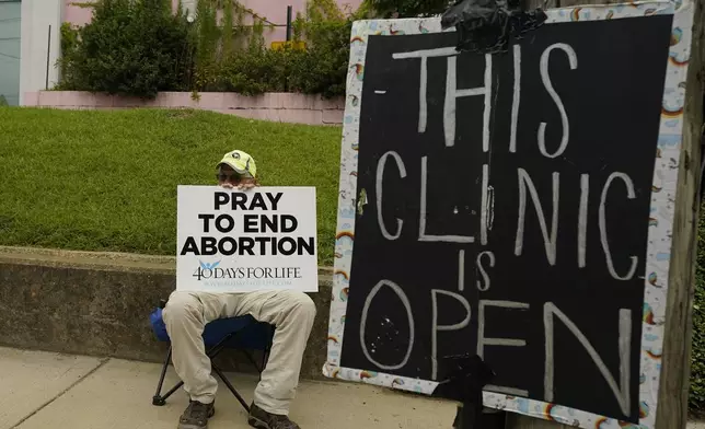 FILE - An anti-abortion supporter sits behind a sign that advises the Jackson Women's Health Organization clinic is still open in Jackson, Miss., July 6, 2022. (AP Photo/Rogelio V. Solis, File)