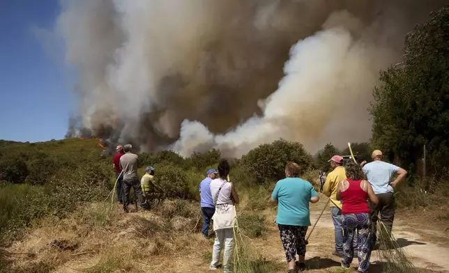 Residents watch as a fire advances toward Rebordondo village, near Ourense, in northwestern Spain, on Monday, Aug. 18, 2025. (AP Photo/Pablo Garcia)