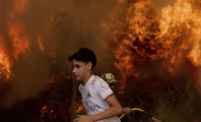 A resident runs past the flames as they try to put out the fire near Rebordondo village, close to Ourense, in northwestern Spain, on Monday, Aug. 18, 2025. (AP Photo/Pablo Garcia)