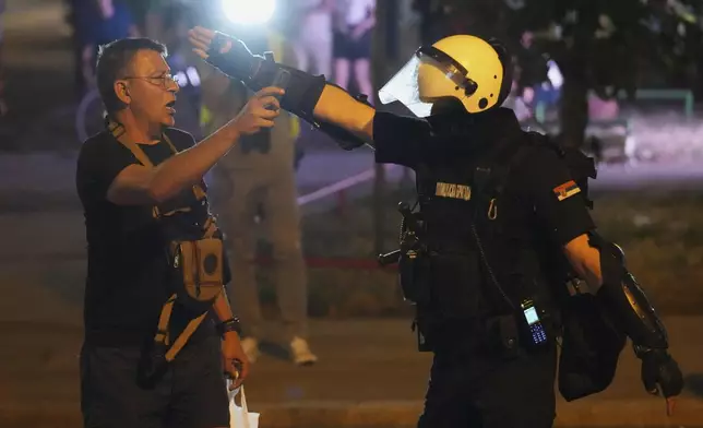 A Serbian riot police officer directs a man filming after clearing people blocking a street during an anti-government protest in Belgrade, Serbia, Saturday, Aug. 16, 2025. (AP Photo/Darko Vojinovic)