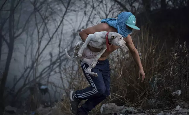 A man, holding a dog, runs from a blaze raging through a neighborhood of Salta, Argentina, Friday, Aug. 1, 2025. (AP Photo/Javier Corbalan)