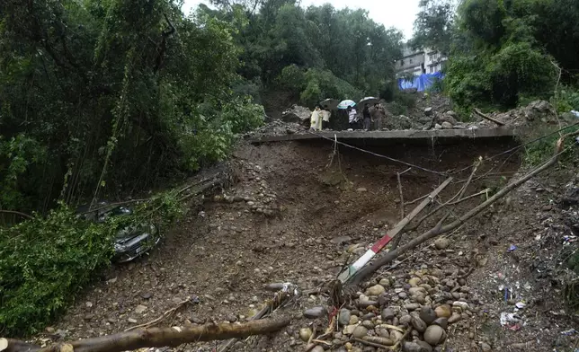 People look at the remains of a road damaged by flash floods in Jammu, India, Wednesday, Aug. 27, 2025. (AP Photo/Channi Anand)