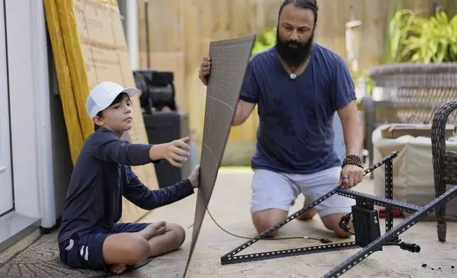 Bhavin Misra, right, and his son, Rumi, 10, assemble a Craftstrom Solar plug-in kit at their home Tuesday, Aug. 5, 2025, in Houston. (AP Photo/David J. Phillip)