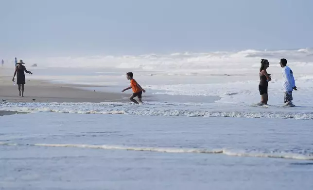 People are seen in the water as waves from Hurricane Erin crash along beach in Duck, N.C., on Tuesday, Aug. 19, 2025. (AP Photo/Pablo Martinez Monsivais)