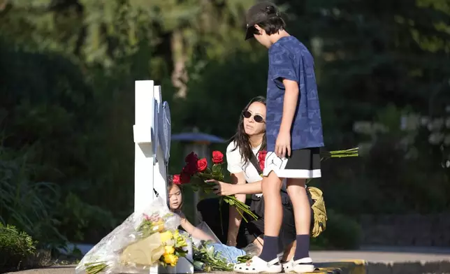 Amy Dols, and her children, Archie and Paloma place flowers at a memorial at Annunciation Catholic Church after Wednesday's school shooting, Thursday, Aug. 28, 2025, in Minneapolis. (AP Photo/Abbie Parr)