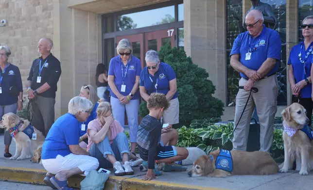 Members of a Lutheran church charities comfort dog ministry sit and stand in front of the Annunciation Catholic Church after Wednesday's school shooting, Thursday, Aug. 28, 2025, in Minneapolis. (AP Photo/Abbie Parr)