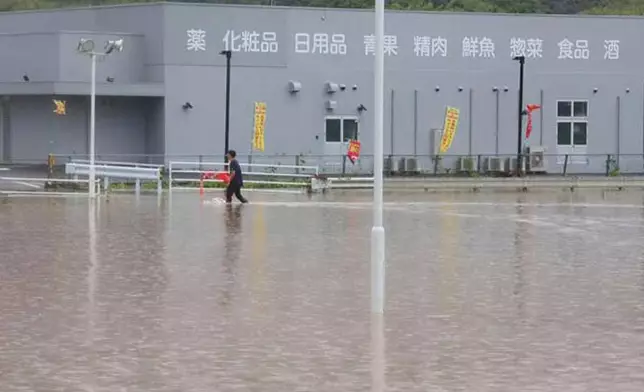 A person walks through a flooded parking lot of a store in Kumamoto, southern Japan Monday, Aug. 11, 2025. (Kyodo News via AP)