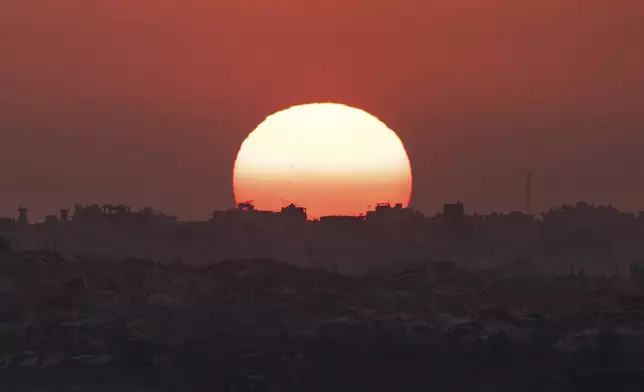 The sun sets behind buildings destroyed during Israeli ground and air operations in the Gaza Strip, as seen from southern Israel, Friday, Aug. 29, 2025. (AP Photo/Maya Levin)