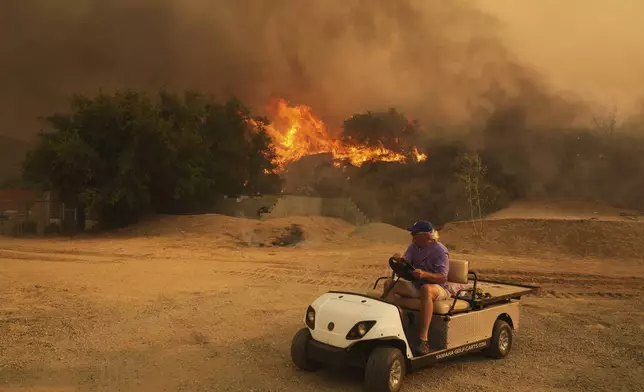 A resident rides a golf cart as he exits his property while the Canyon Fire burns on Thursday, Aug. 7, 2025, in Hasley Canyon, Calif. (AP Photo/Marcio Jose Sanchez)