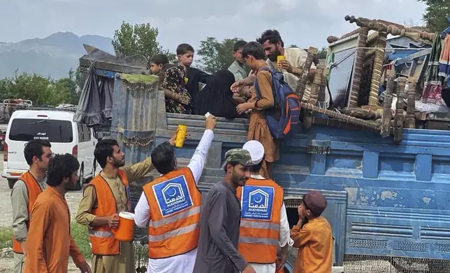 Volunteers offer water to Internally Displaced People, who flee from their homes due to security forces launched a targeted operation against militants, at a highway near Khar, the main town of Bajaur, a northwestern Pakistani district bordering Afghanistan, Monday, Aug. 11, 2025. (AP Photo/Anwarullah Khan)