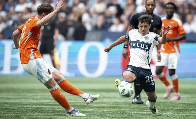 Houston Dynamo's Jack McGlynn kicks the ball as Vancouver Whitecaps' Andres Cubas (20) defends during the first half of an MLS soccer match in Vancouver, British Columbia, Sunday, Aug. 17, 2025. (Ethan Cairns/The Canadian Press via AP)