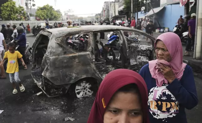 People inspect the wreckages of cars burned in violent protests against lawmakers' allowance and alleged police brutality after a delivery rider was run over by a police armored vehicle during clashes between riot police and students protesters, in Jakarta, Indonesia, Saturday, Aug. 30, 2025. (AP Photo/Dita Alangkara)