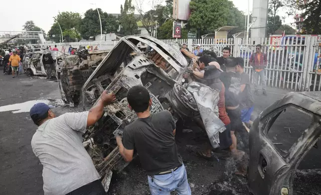 People overturn the wreckage of a car burned in violent protests against lawmakers' allowance and alleged police brutality after a delivery rider was run over by a police armored vehicle during clashes between riot police and students protesters, in Jakarta, Indonesia, Saturday, Aug. 30, 2025. (AP Photo/Dita Alangkara)