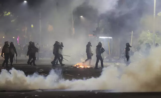 Police officers walk amid tear gas smoke during a protest in Surabaya, East Java, Indonesia, Saturday, Aug. 30, 2025, sparked by reports of lawmakers receiving excessive housing allowances. (AP Photo/Trisnadi)