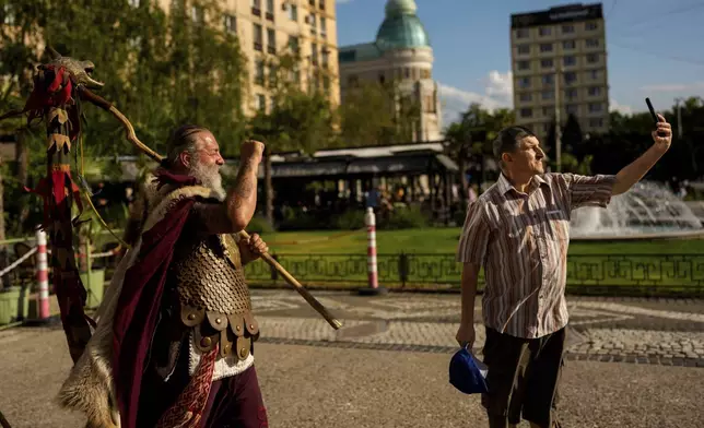 Constantin "The Castor" Lapusneanu, wearing a Dacian warrior outfit, clenches his fist as a man takes a selfie photograph in Iasi, Romania, Friday, July 11, 2025 ahead of the Getodava historical reenactment festival. (AP Photo/Andreea Alexandru)