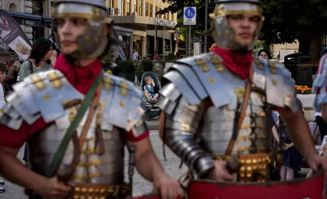 A baby sits in a stroller behind men wearing Roman soldiers outfits in Iasi, Romania, Friday, July 11, 2025 ahead of the Getodava historical reenactment festival. (AP Photo/Andreea Alexandru)