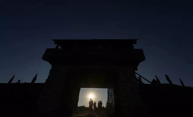 People are silhouetted by the setting sun as they walk around a replica of a Getic fortress in Poiana, Romania, Saturday, July 12, 2025, during the Getodava historical reenactment festival. (AP Photo/Andreea Alexandru)