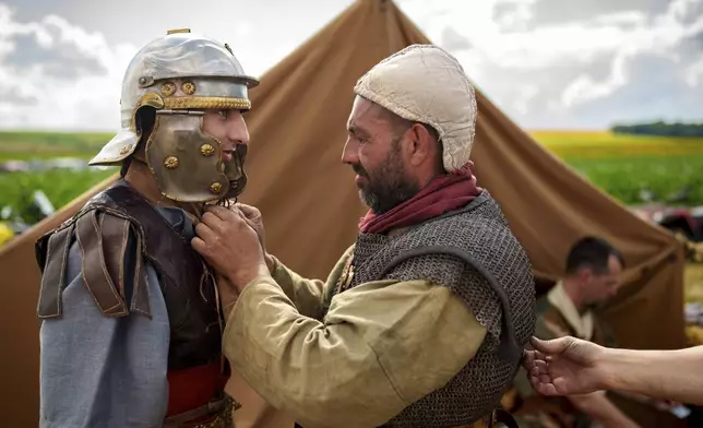 Ondrej Kohut, left, of the Legio X Gemina Coh II, Roman era military historical group with members from the Czech Republic and Slovakia, has his Roman soldier outfit adjusted by colleague Ludovic Kohut in Poiana, Romania, Saturday, July 12, 2025, during the Getodava historical reenactment festival. (AP Photo/Vadim Ghirda)