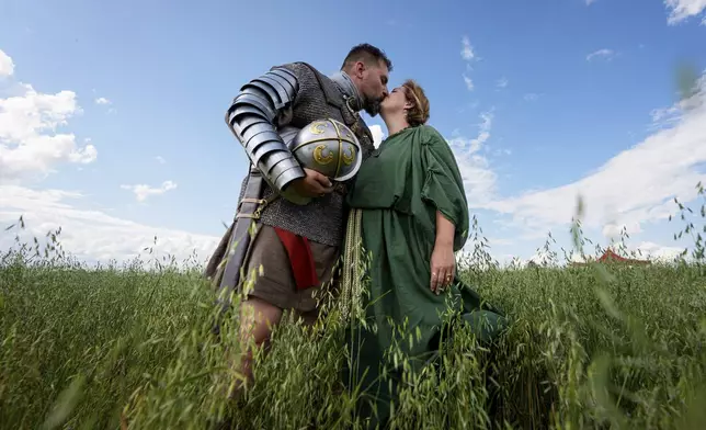 Andrej Miklanek of the Legio X Gemina Coh II, Roman era military historical group with members from the Czech Republic and Slovakia, kisses Valeria Terezia Danciakova after posing for a photograph in Poiana, Romania, Saturday, July 12, 2025, during the Getodava historical reenactment festival. (AP Photo/Andreea Alexandru)