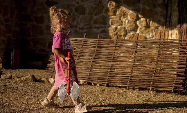 A child walks holding a replica of a battle axe in Poiana, Romania, Sunday, July 13, 2025, during the Getodava historical reenactment festival. (AP Photo/Andreea Alexandru)