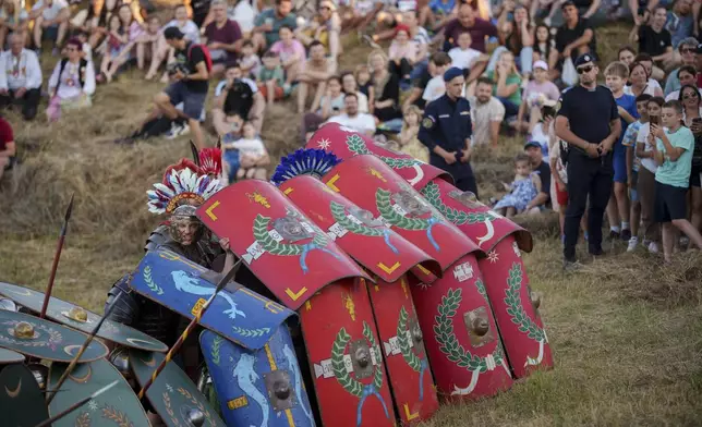 People watch as members of historical reenactment groups wearing Roman soldier outfits, demonstrate Roman era warfare tactics in Poiana, Romania, Saturday, July 12, 2025, during the Getodava historical reenactment festival. (AP Photo/Vadim Ghirda)