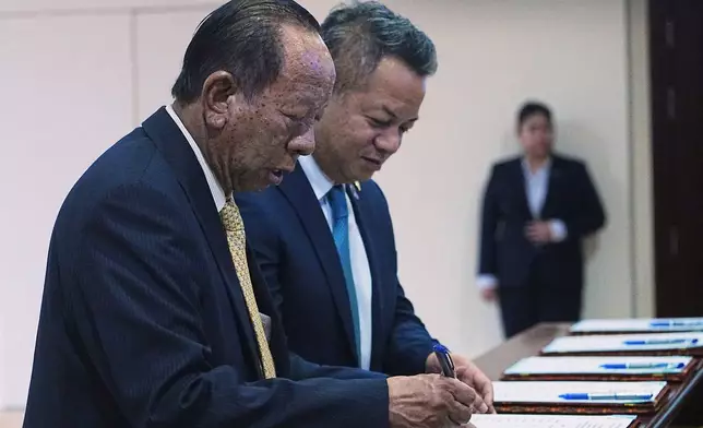 Cambodian lawmaker Tea Banh, left, registers together with his son, Deputy Prime Minister and Minister of National Defense Tea Seiha, center, before the session on the draft law on amending the law on nationality at the National Assembly in Phnom Penh Cambodia, Monday, Aug. 25, 2025. (AP Photo/Heng Sinith)