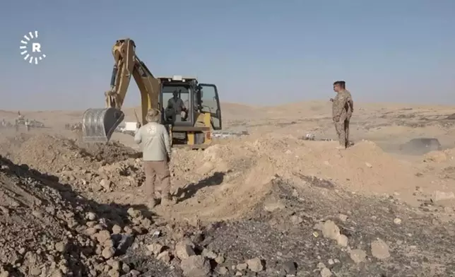 In this image taken from video provided by Rudaw TV, workers dig out human remains at the Khasfa site near the northern Iraqi city of Mosul, where authorities have begun excavating a mass grave believed to contain thousands of victims of the Islamic State (IS) Mosul, Iraq, Sunday, Aug. 17, 2025. (Rudaw TV via AP)
