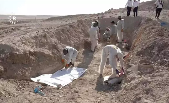 In this image taken from video provided by Rudaw TV, workers dig out human remains at the Khasfa site near the northern Iraqi city of Mosul, where authorities have begun excavating a mass grave believed to contain thousands of victims of the Islamic State (IS) Mosul, Iraq, Sunday, Aug. 17, 2025. (Rudaw TV via AP)