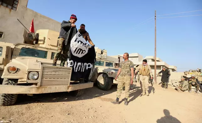 FILE - Iraqi Army soldiers celebrate as they hold a flag of the Islamic State group they captured during a military operation to regain control of a village outside Mosul, Iraq, Tuesday, Nov. 29, 2016. Iraqi officials have begun excavation of what is believed to be a mass grave left behind by the Islamic State extremist group during its rampage across the country a decade ago. (AP Photo/Hadi Mizban, File)