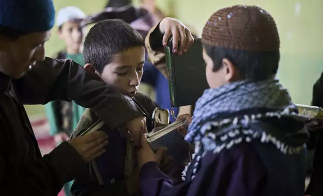 An Afghan boy hands out Qurans to fellow students at the Imam al-Tirmidhi religious school in Kabul, Afghanistan, Wednesday, June 11, 2025. (AP Photo/Ebrahim Noroozi)