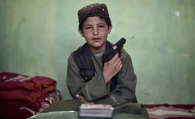 An Afghan boy poses for a photo with his toy pistol at the Imam al-Tirmidhi religious school in Kabul, Afghanistan, Wednesday, June 11, 2025. (AP Photo/Ebrahim Noroozi)