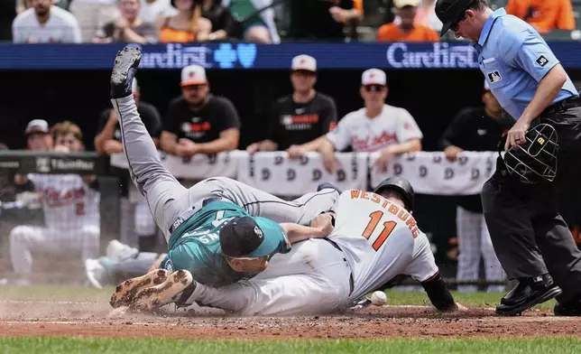 Baltimore Orioles' Jordan Westburg (11) scores past Seattle Mariners starting pitcher Logan Evans, left, on a wild pitch and fielding error by Evans during the fourth inning of a baseball game, Thursday, Aug. 14, 2025, in Baltimore. (AP Photo/Stephanie Scarbrough)