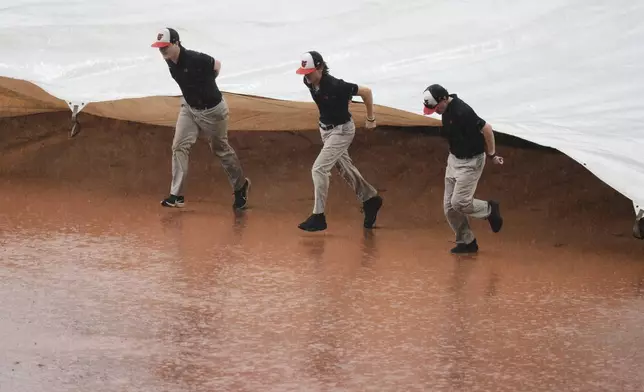 Members of the grounds crew place a tarp over the infield during a rain delay in the sixth inning of a baseball game between the Baltimore Orioles and the Seattle Mariners, Thursday, Aug. 14, 2025, in Baltimore. (AP Photo/Stephanie Scarbrough)