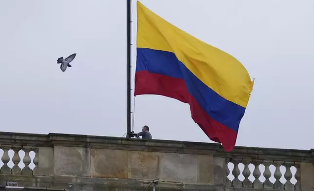 A worker raises the flag to fly at half-staff at Congress in Bogota, Colombia, after the announcement of the death of opposition Sen. and presidential hopeful Miguel Uribe, more than two months after he was shot during a campaign rally, Monday, Aug. 11, 2025. (AP Photo/Fernando Vergara)