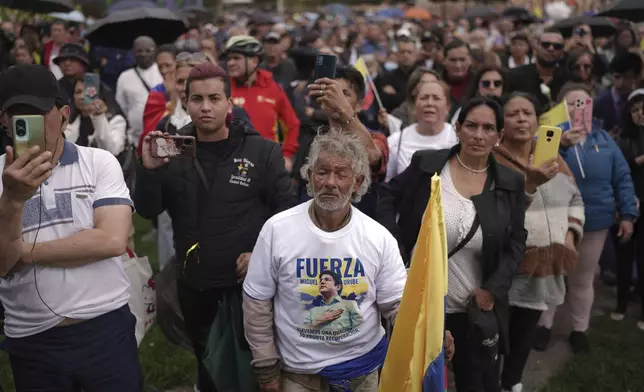 People watch the funeral of presidential hopeful and opposition Sen. Miguel Uribe, who died from wounds suffered when he was shot at a political rally, on a screen outside the cemetery in Bogota, Colombia, Wednesday, Aug. 13, 2025. (AP Photo/Ivan Valencia)