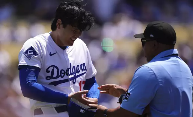 Los Angeles Dodgers' Shohei Ohtani, left, laughs while being checked by the third base umpire after pitching in the first inning of a baseball game against the St. Louis Cardinals, Wednesday, Aug. 6, 2025, in Los Angeles. (AP Photo/Mark J. Terrill)