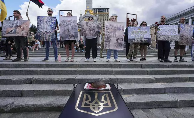 People hold works of David Chichkan, a Ukrainian serviceman and artist during his farewell ceremony at Independence square in Kyiv, Ukraine, on Monday, Aug. 18, 2025. (AP Photo/Evgeniy Maloletka)