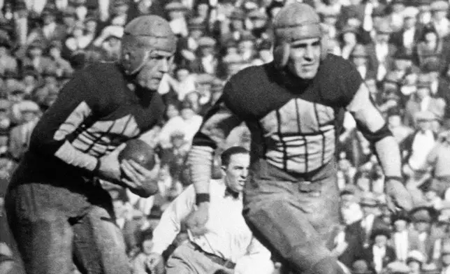 FILE - Illinois' Red Grange, left, follows a blocker on a 95-yard kickoff return for a touchdown against Michigan during a college football game on Oc.t 18, 1924, in Champaign, Ill. (AP Photo/File)