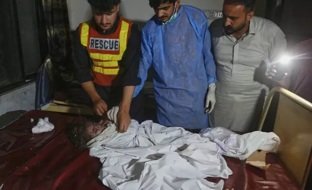 A paramedic and others look at the body of a child, who was killed in the flash flooding at a local hospital in Pir Baba, in Buner district, in Pakistan's northwest, Friday, Aug. 15, 2025. (AP Photo/Muhammad Sajjad)