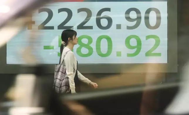A person, seen through a car window. walks in front of an electronic stock board showing Japan's Nikkei index at a securities firm Tuesday, Aug. 26, 2025, in Tokyo. (AP Photo/Eugene Hoshiko)