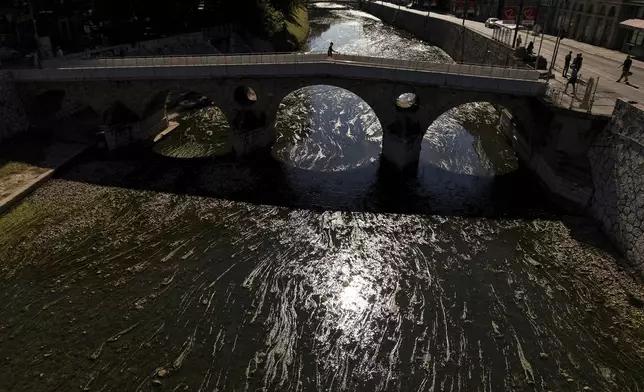 A person walks on a bridge over the Miljacka River, which is almost dried-up with algae visible, amid a heatwave and drought in Sarajevo, Bosnia, Sunday, Aug. 10, 2025. (AP Photo/Armin Durgut)