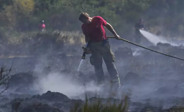 Members of the London Fire Brigade tackle a wildfire on Wanstead Flats in London, Tuesday, Aug. 12, 2025. (AP Photo/Joanna Chan)