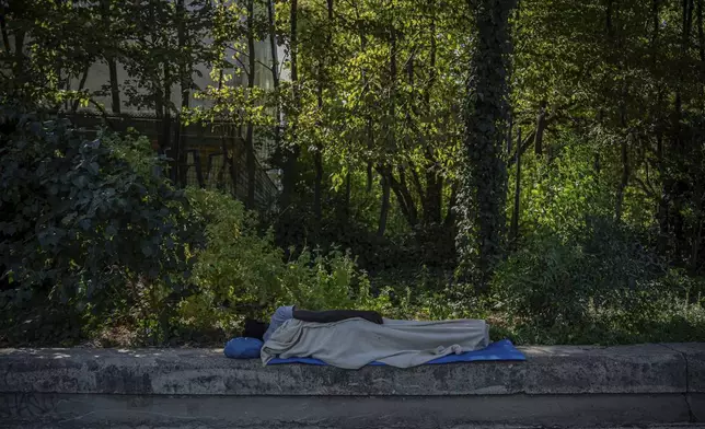 A homeless man sleeps in the shade of a tree, Tuesday, Aug. 12, 2025 in Paris. (AP Photo/Aurelien Morissard)