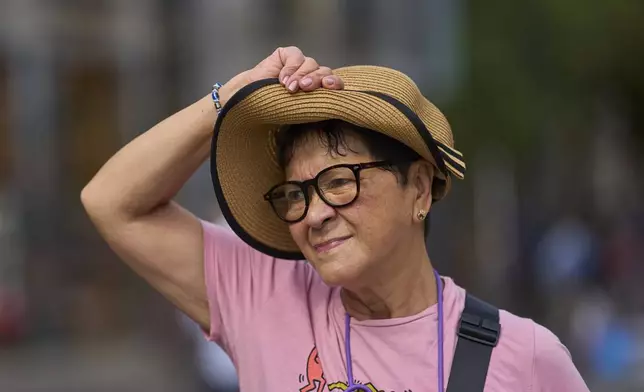 A woman protects herself with her hat during a heat wave in Madrid, Spain, Tuesday, Aug. 12, 2025. (AP Photo/Manu Fernandez)