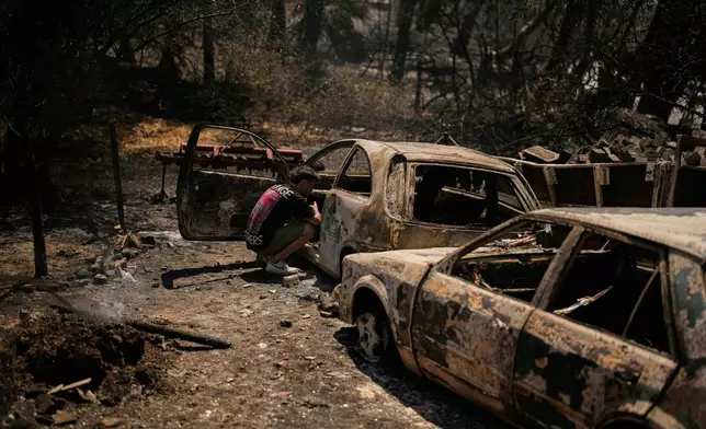 A man checks a burned car after a fire in Guzelyeli, outskirts Canakkale, northwest Turkey, Tuesday, Aug. 12, 2025. (AP Photo/Khalil Hamra)