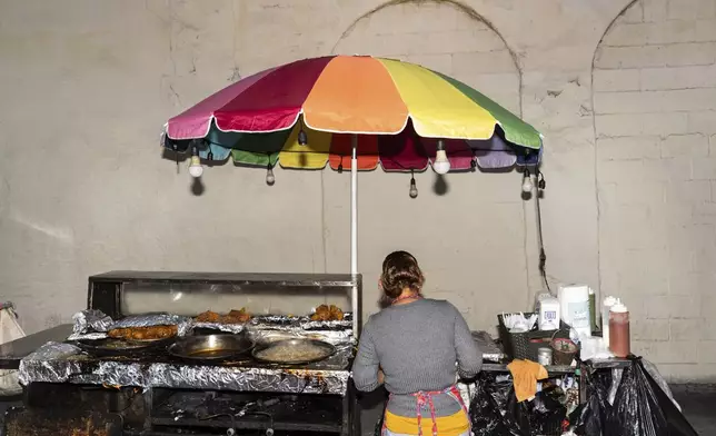Street vendor Francisca, an immigrant from Guatemala, prepares an order at her cart in Los Angeles, Tuesday, Aug. 5, 2025, where her son accompanies her to help monitor their surroundings amid ongoing ICE raids. (AP Photo/Jae C. Hong)